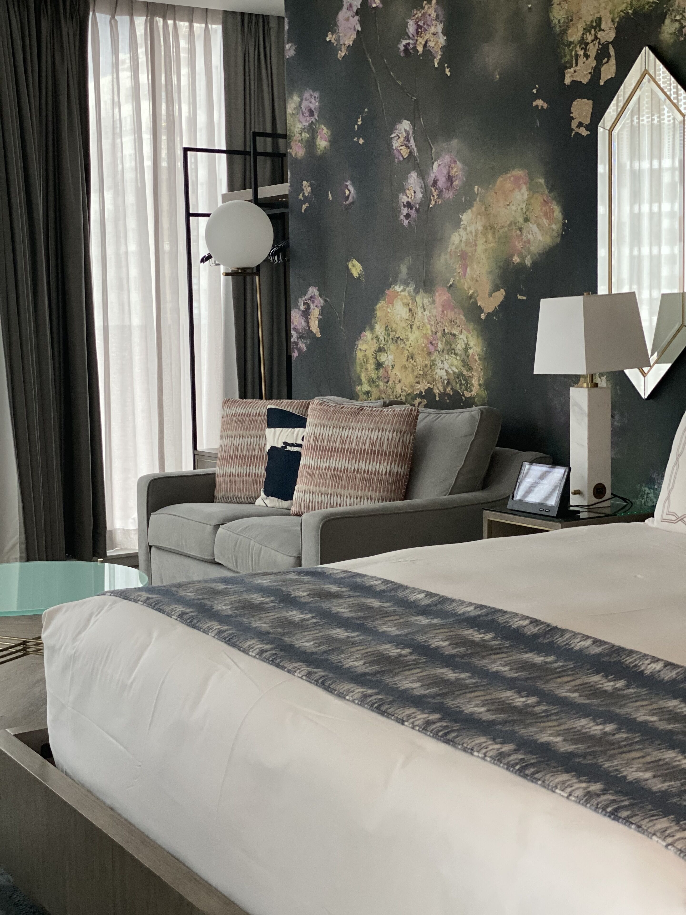 A hotel room with a bed, a sofa, a desk, and a large window with curtains.