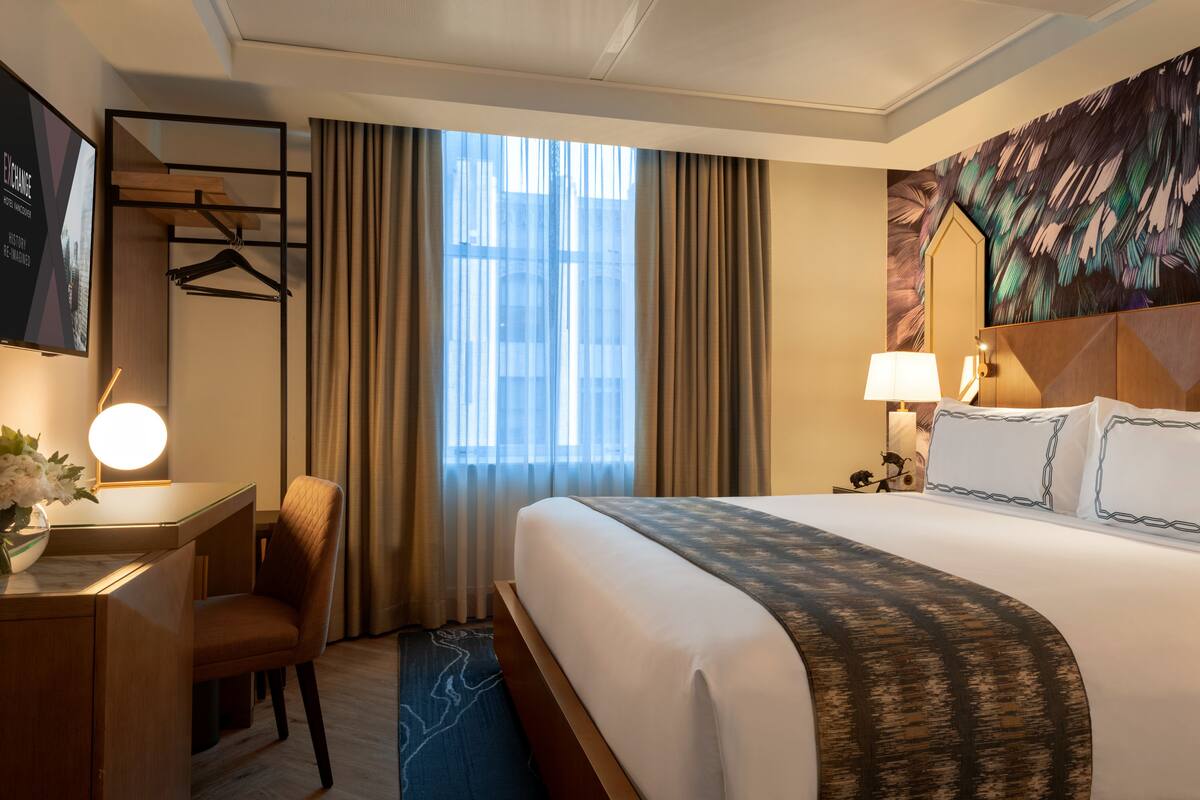 A hotel room with a bed, a desk with a lamp, a chair, a TV, and a window with curtains.