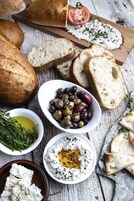 Una mesa de madera rústica con diversos alimentos, como pan, aceitunas y cuencos de salsas.