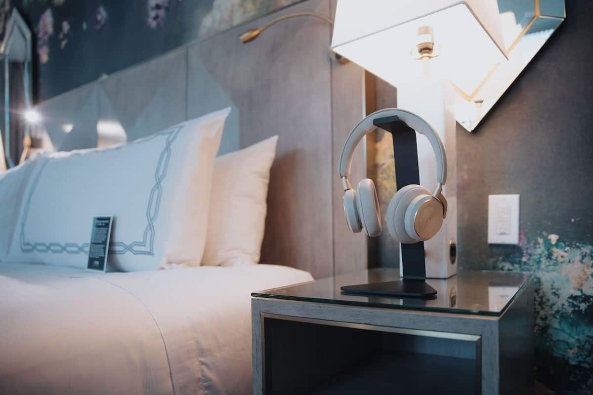 A neatly made bed with a pillow featuring a geometric design, a bedside table with a pair of headphones, and a wall-mounted lamp.