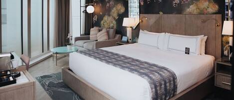 A hotel room with a large bed, a desk, a chair, a small table, and a wall with floral wallpaper.