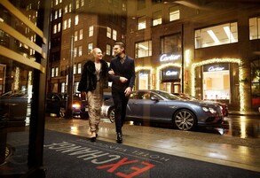 Two people walking past a hotel entrance with a sign that reads "Cartier."