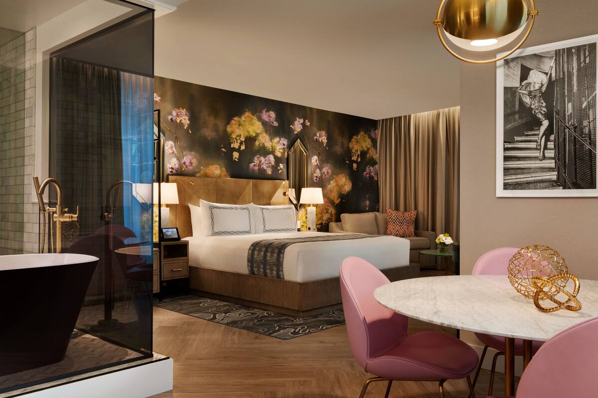 A modern hotel room with a large bed, a round dining table, and a glass-enclosed shower area.