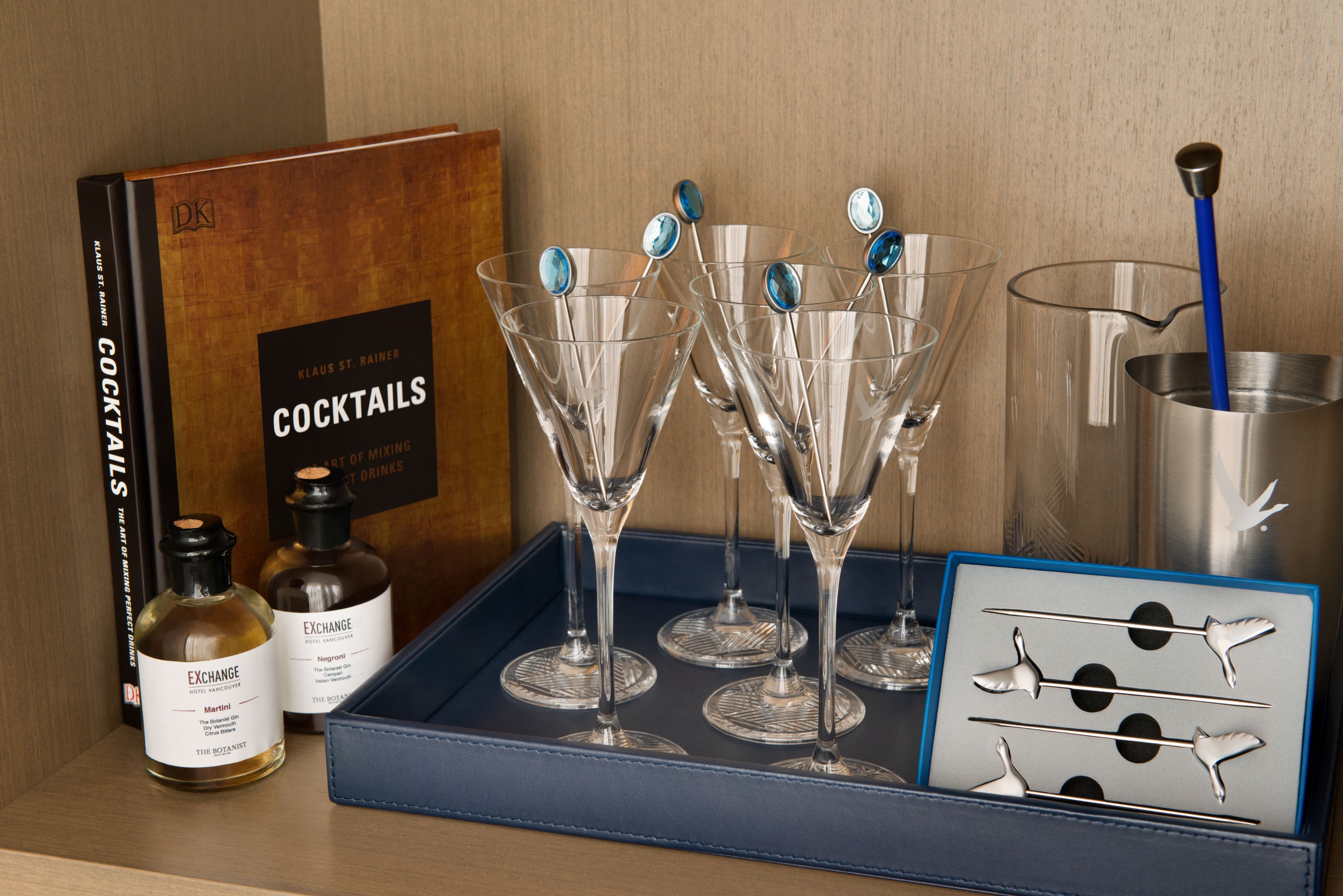 A tray with four martini glasses, two bottles of Martini, a cocktail book, and a set of cocktail stirrers.