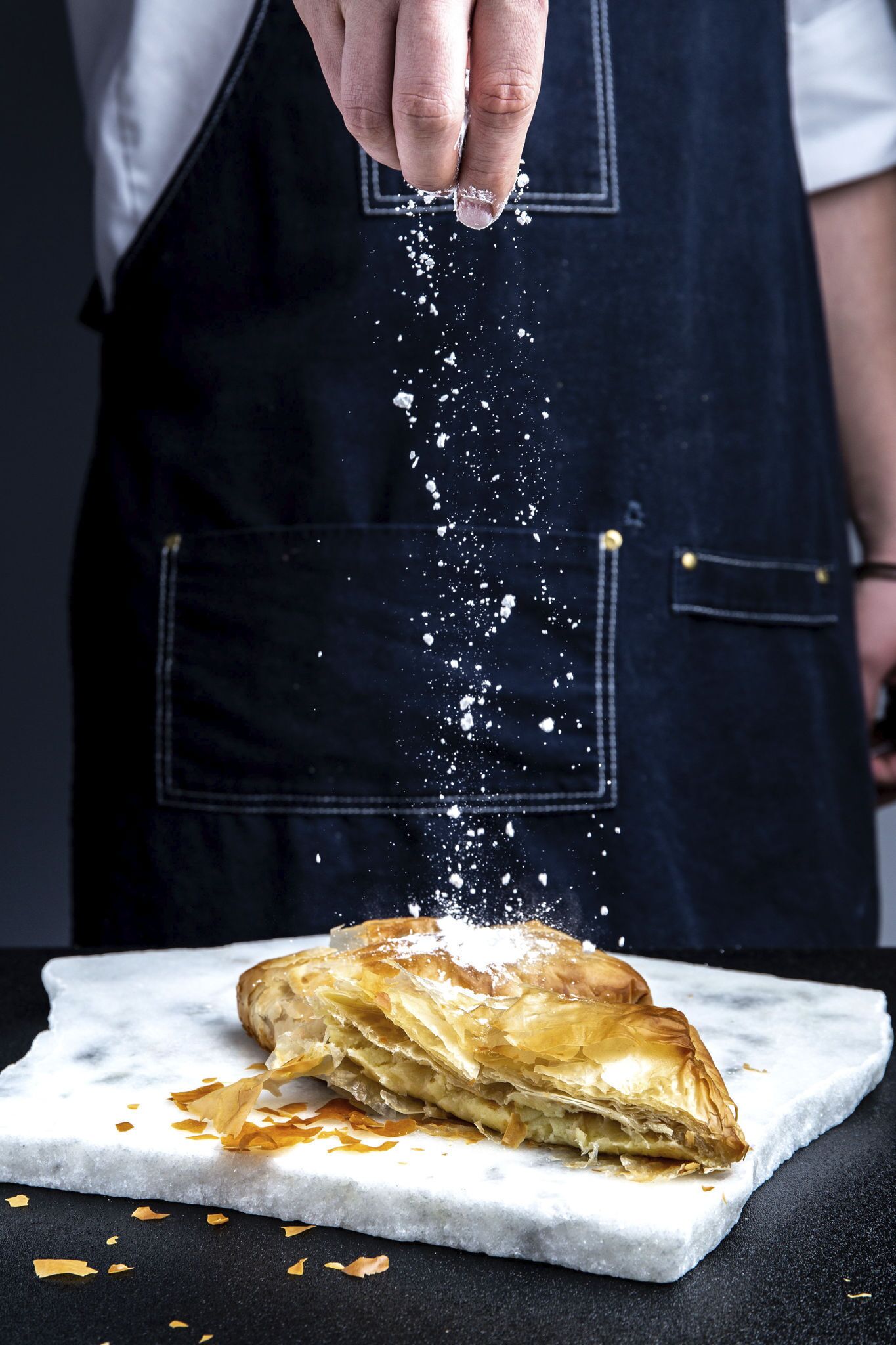 A person sprinkling salt over a pastry on a marble surface.
