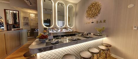 A modern bar area with a marble countertop, multiple stools, and a large mirror with illuminated edges.