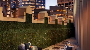 A rooftop terrace with wicker furniture and a view of a modern building with illuminated windows. - EXchange Hotel Vancouver (Vancouver)