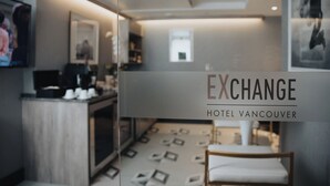 A hotel room with a modern design, featuring a glass partition, a small seating area, and a visible kitchenette. - EXchange Hotel Vancouver (Vancouver)