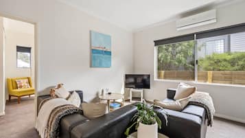 A modern living room with a sofa, a coffee table, a TV, and a large window with a view of greenery.