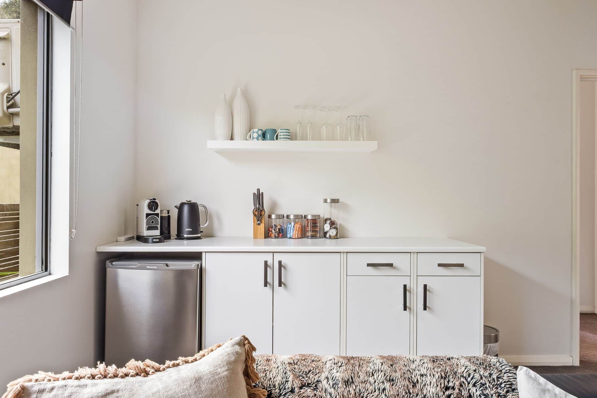 A compact kitchen with a dishwasher, a coffee machine, and a small countertop with jars and utensils.