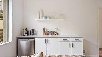 A compact kitchen with a dishwasher, a coffee machine, and a small countertop with jars and utensils.