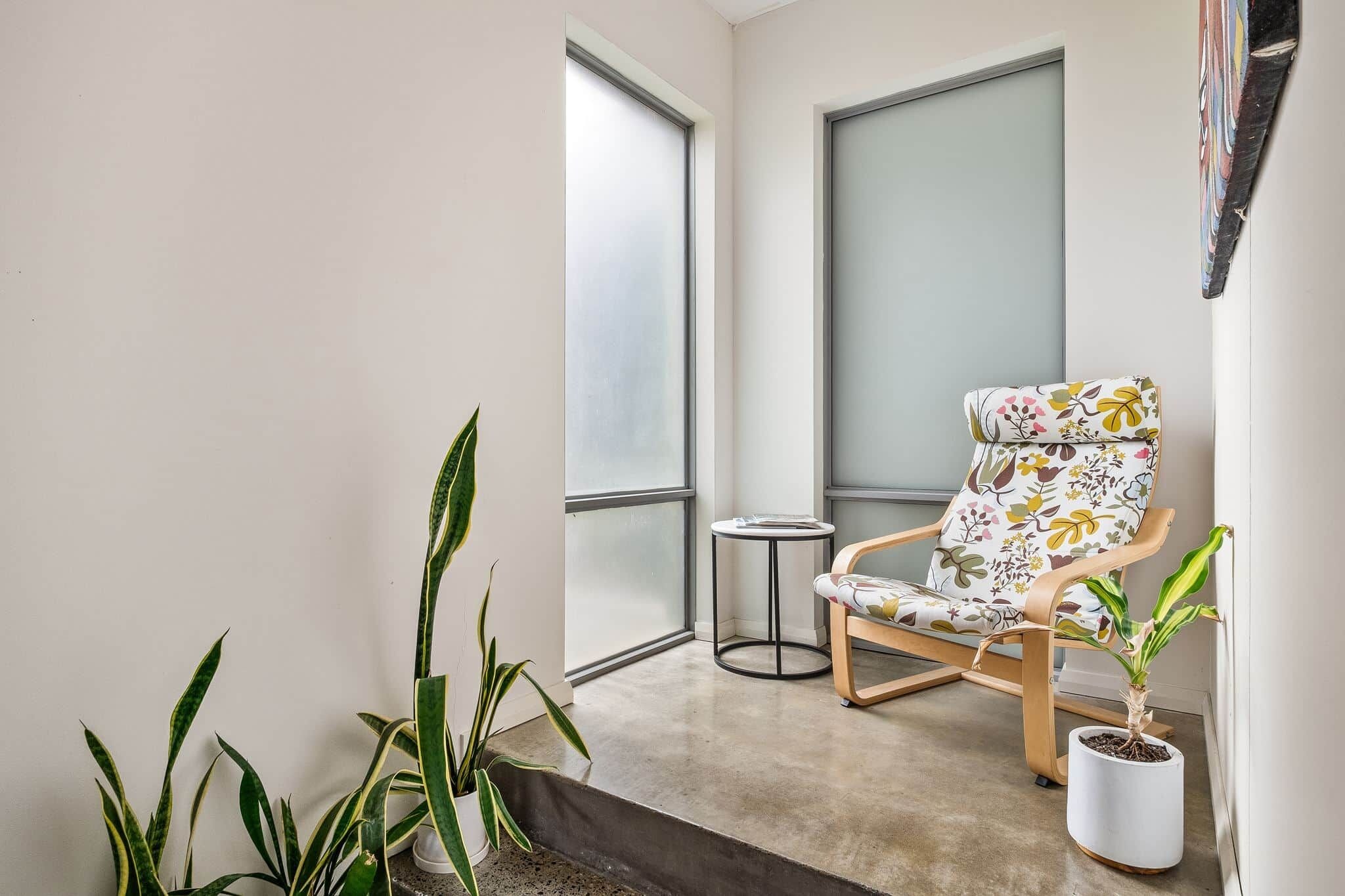 A balcony with a chair, potted plants, and a view through a frosted glass door.
