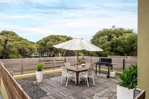 Un patio al aire libre con mesa y sillas, una parrilla y una planta en maceta.