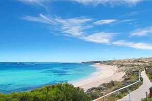 Un paisaje costero con cielo despejado, una playa arenosa y un camino que lleva a la orilla.