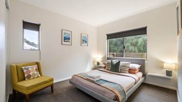 A bedroom with a bed, a yellow armchair, two wall-mounted lamps, and two framed pictures.