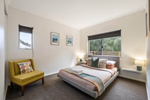 Un dormitorio con una cama, un sillón amarillo, dos lámparas de pared y dos cuadros enmarcados.