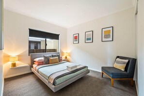 Quarto com cama, cadeira, mesa de cabeceira, luminária e obras de arte na parede.