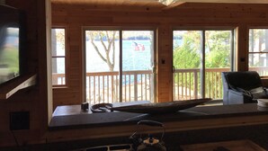 Une cabane dotée d’un coin cuisine, d’une grande fenêtre donnant sur un plan d’eau et d’une terrasse avec vue sur l’eau.