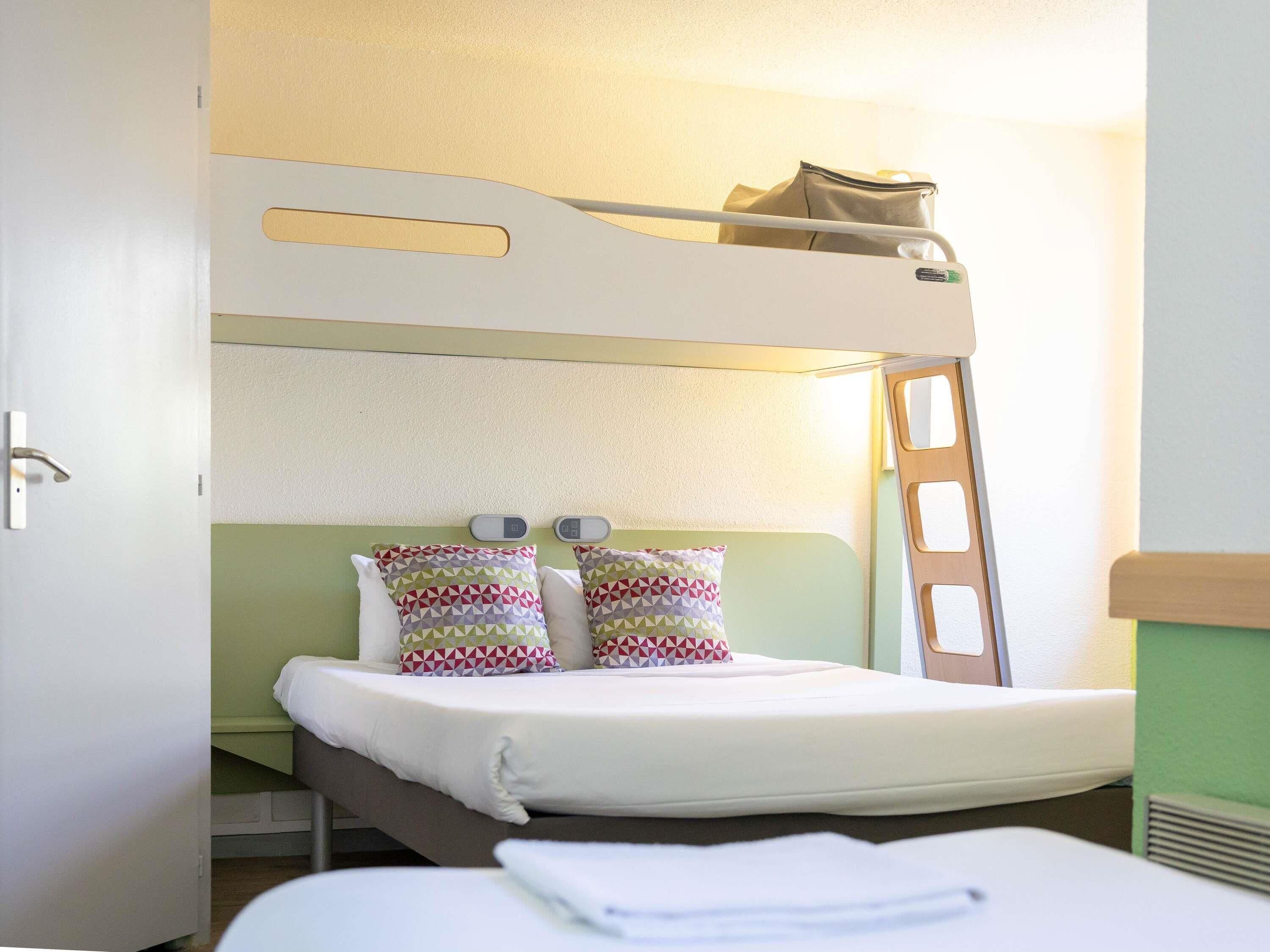 A bunk bed with pillows, a ladder, and a bedside table.