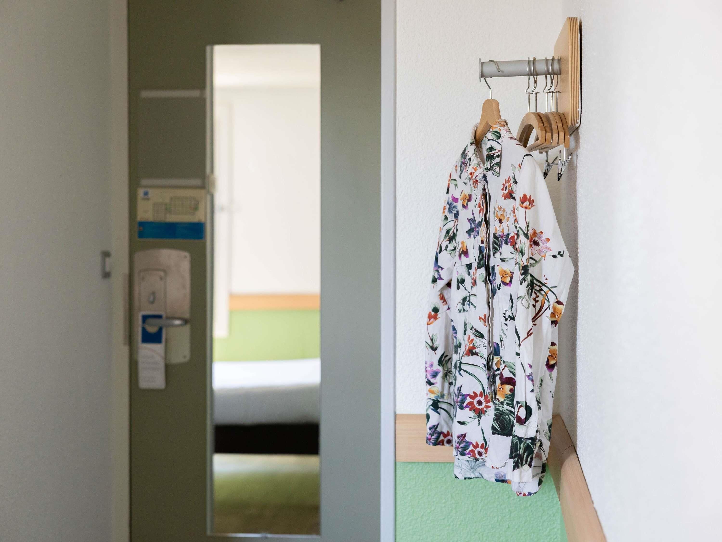 A hallway with a door leading to a room, a mirror, and a rack with floral-patterned robes.