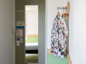 Een hal met een deur naar een kamer, een spiegel en een rek met gewaden met bloemenprint.
