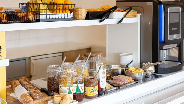 Un buffet de petit-déjeuner comprenant du pain, des fruits, des confitures et une machine à café.