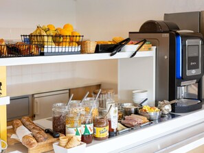 Un bufé de desayuno con pan, frutas, mermeladas y una máquina de café.