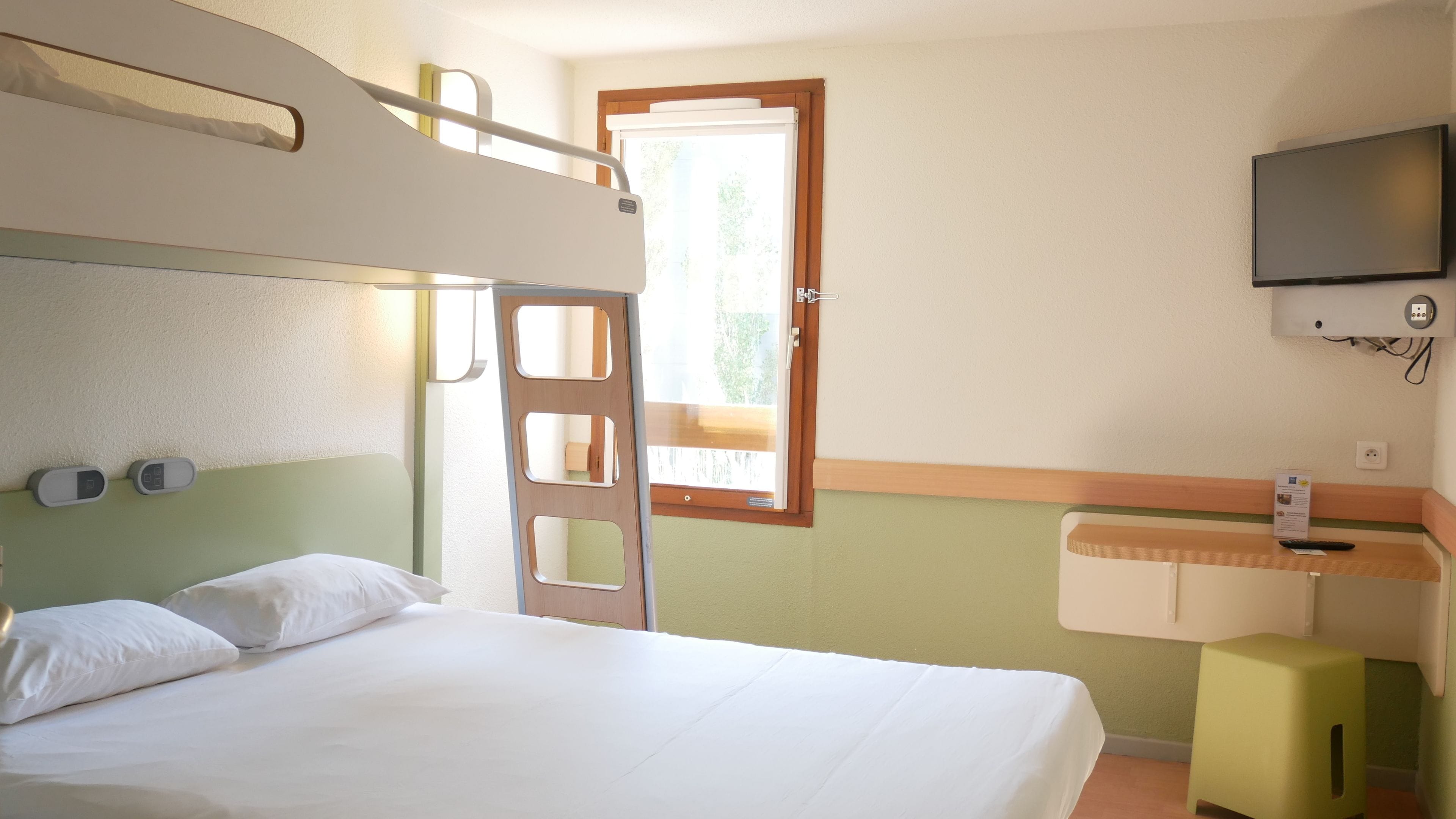 Habitación de hotel con cama, un escritorio pequeño, televisor y ventana con vista a follaje.