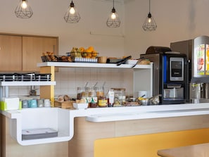 Una cuina moderna amb cafetera, cistella de fruita i diversos aliments.