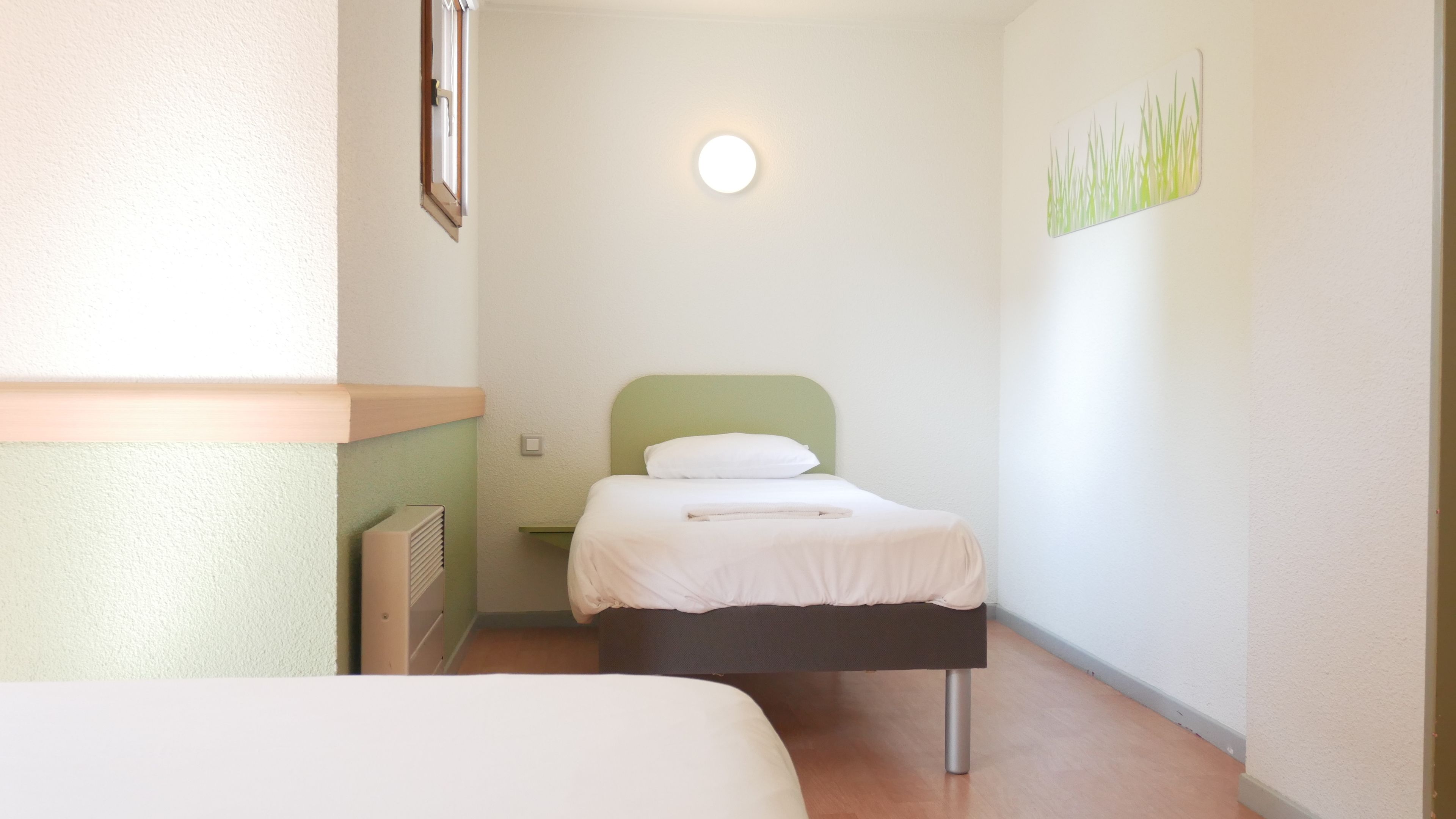Una habitación pequeña y limpia con cama, radiador y luz empotrada en la pared.