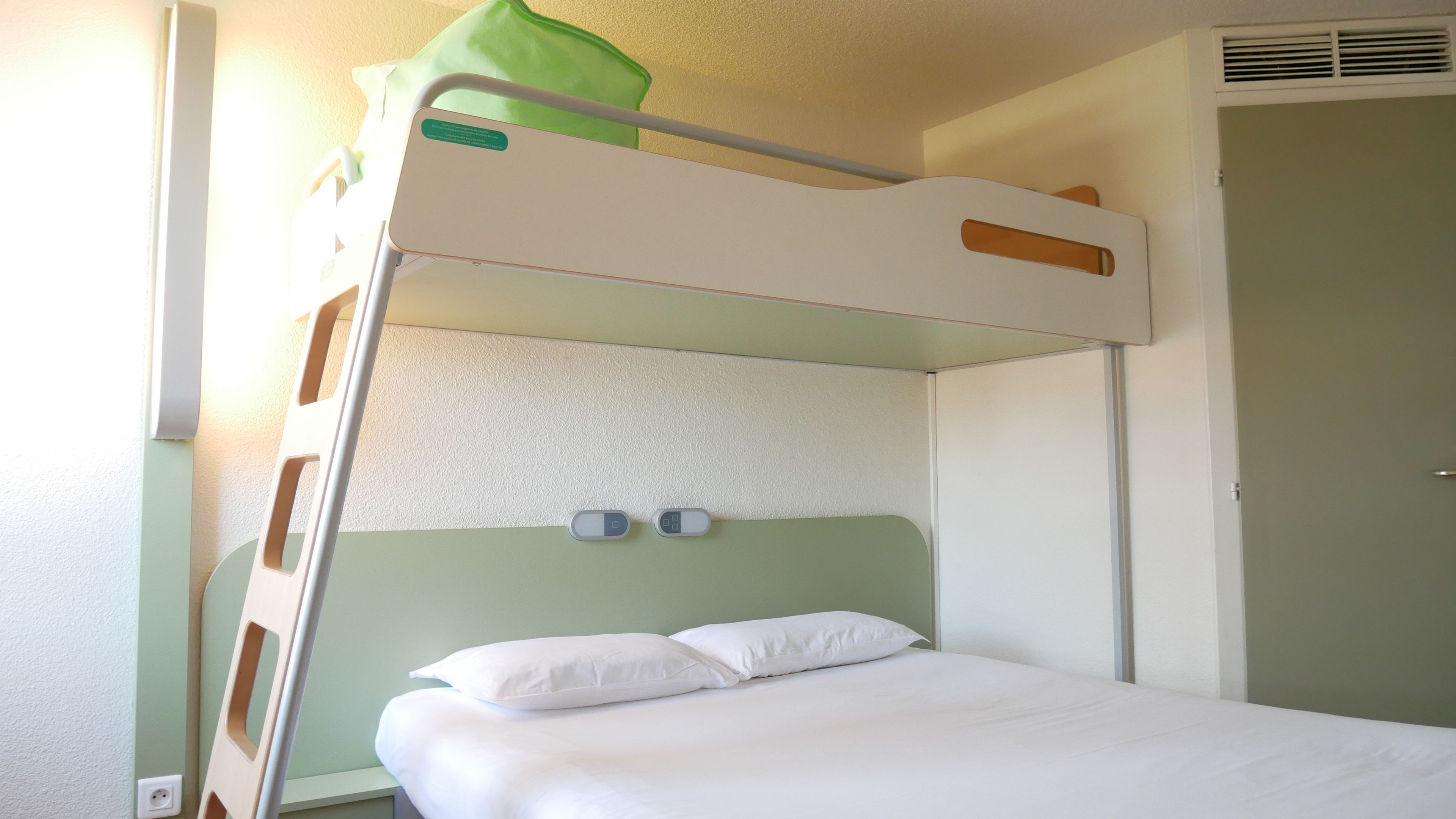 Una cama litera con un almohadón verde arriba, un cabecero blanco y dos mesitas de noche con tazas.