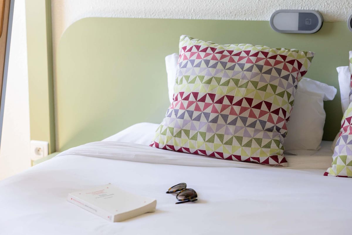 Un lit bien fait, avec un oreiller à motifs, un livre et une paire de lunettes posés sur le lit.