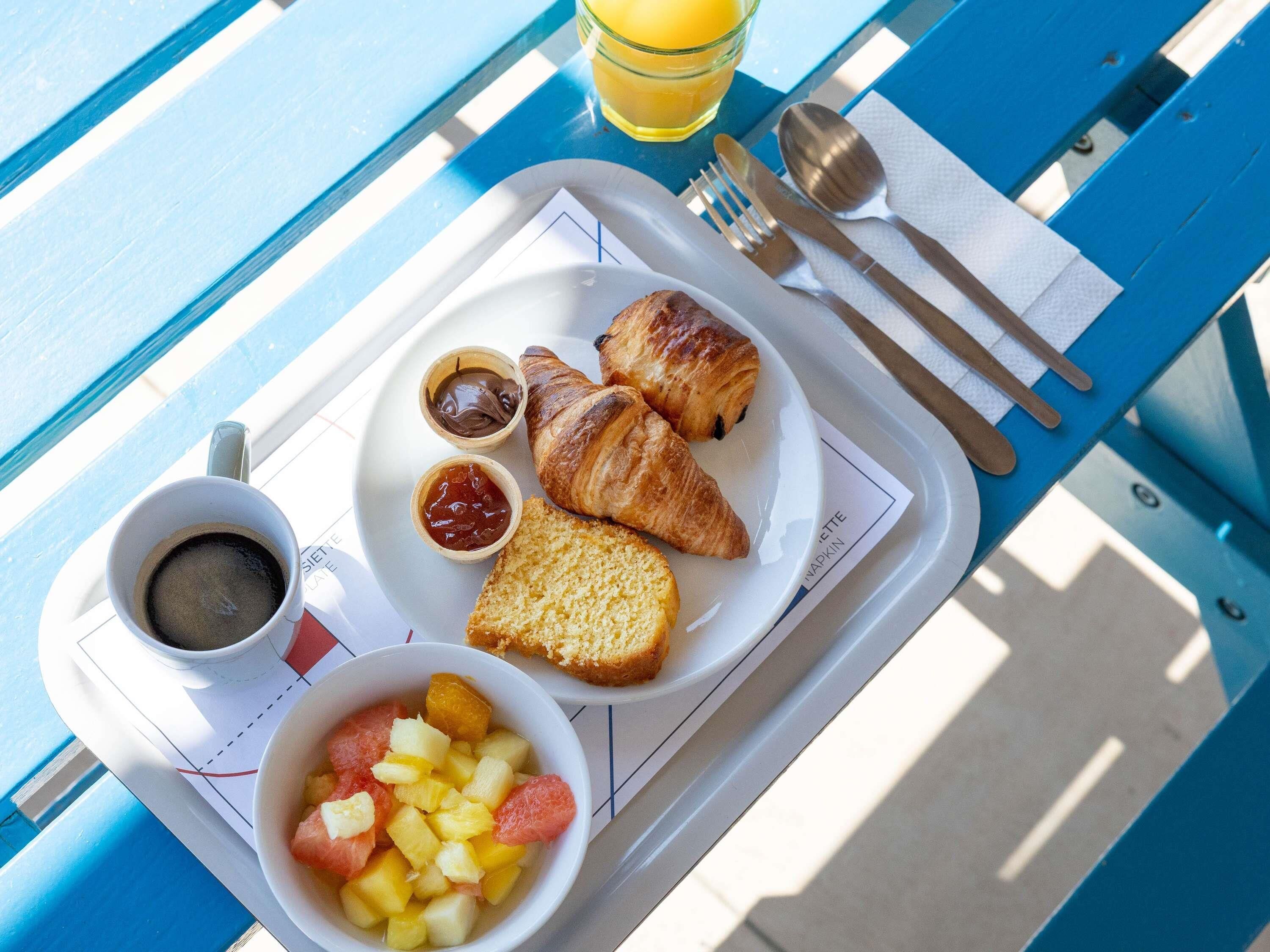 Una bandeja de desayuno con cruasanes, fruta, mermelada y café sobre una mesa azul.