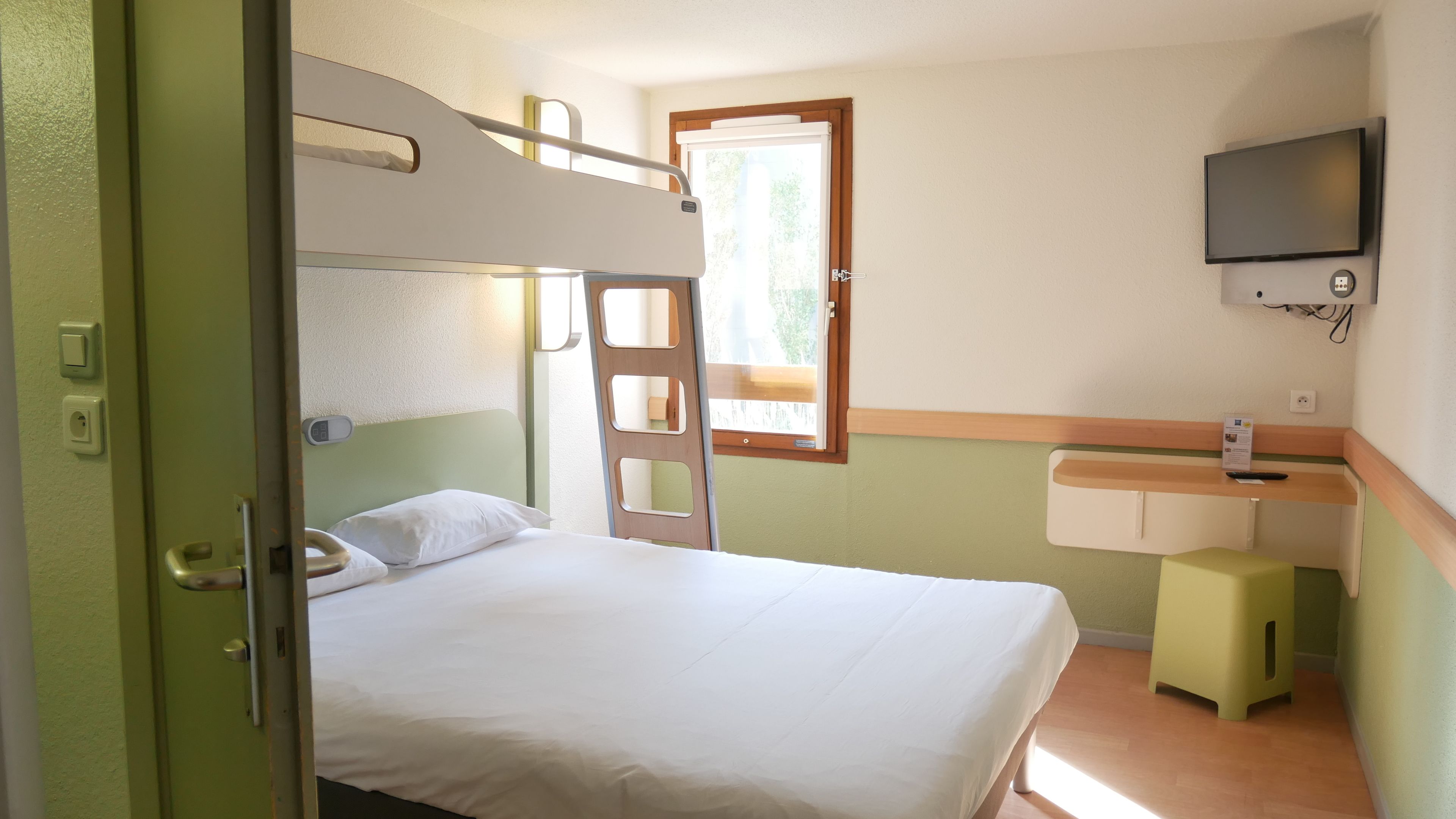 Una cama litera con escritorio y televisión en una habitación con ventana.