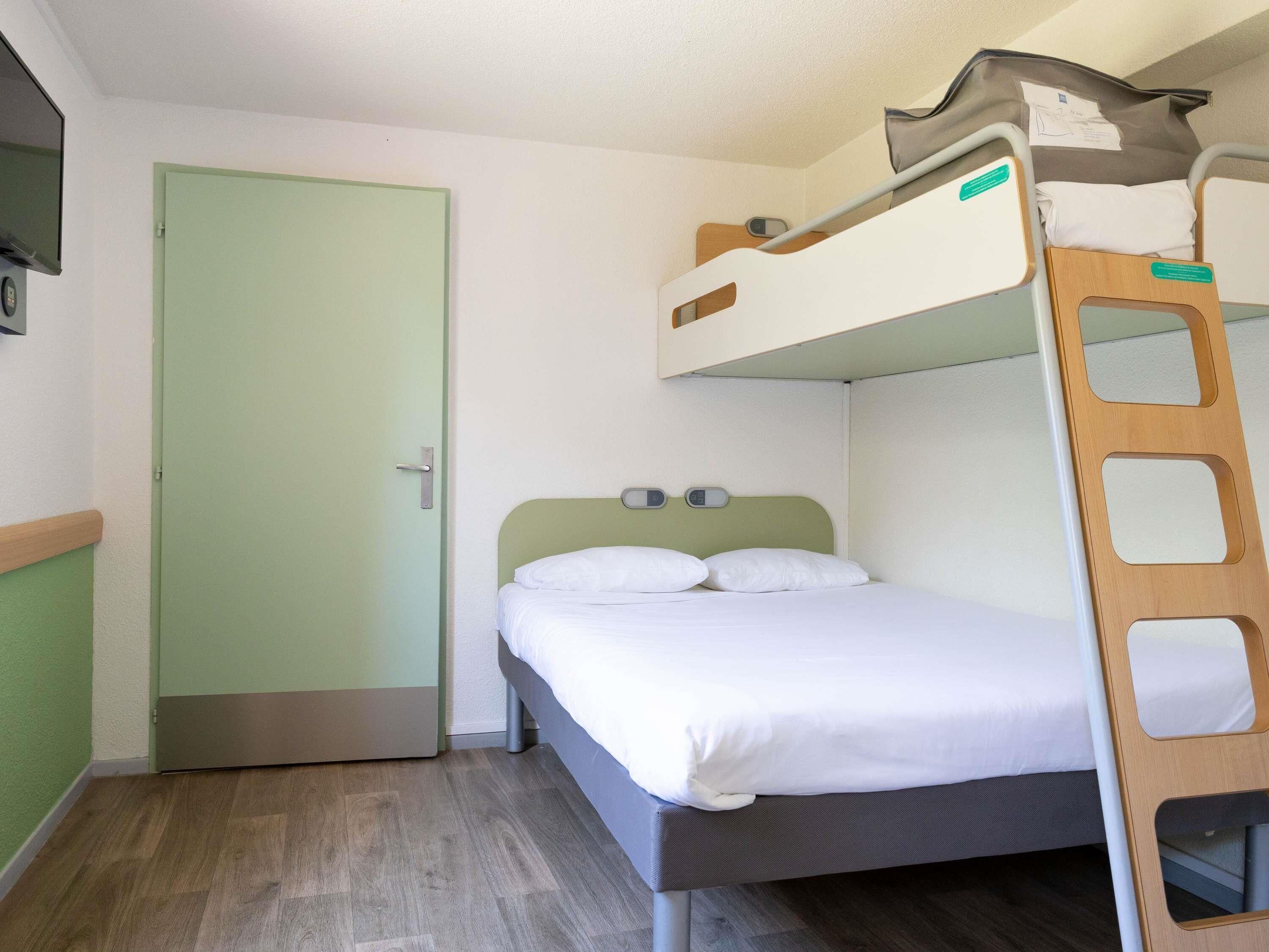 A bunk bed with a ladder, a single bed, a door, and a television on the wall.