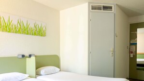 Une chambre d’hôtel avec deux lits, une tête de lit verte, une porte blanche et un climatiseur fixé au mur.