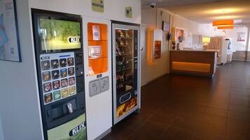 Un espace d’accueil comprenant un distributeur automatique de la marque K-LIX, un comptoir d’accueil et un espace d’attente avec un canapé.