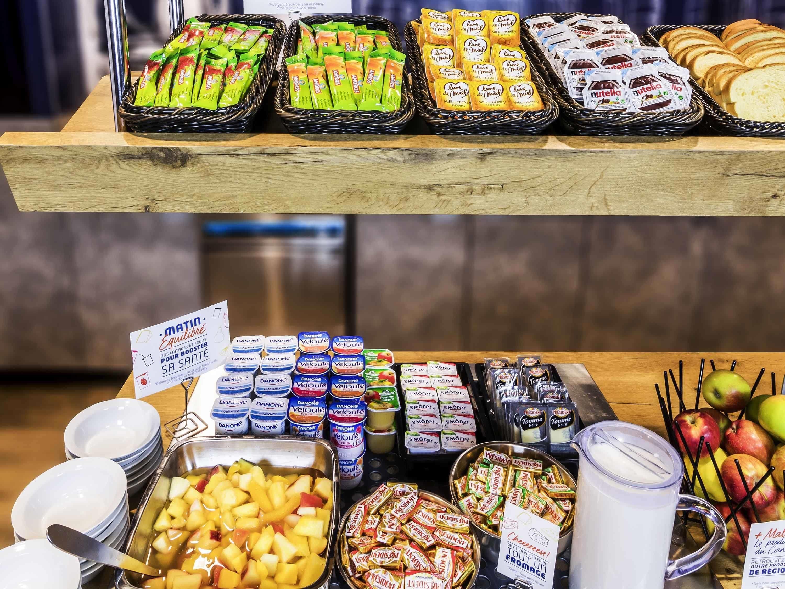 A buffet with various food items including fruits, pastries, and packaged snacks.