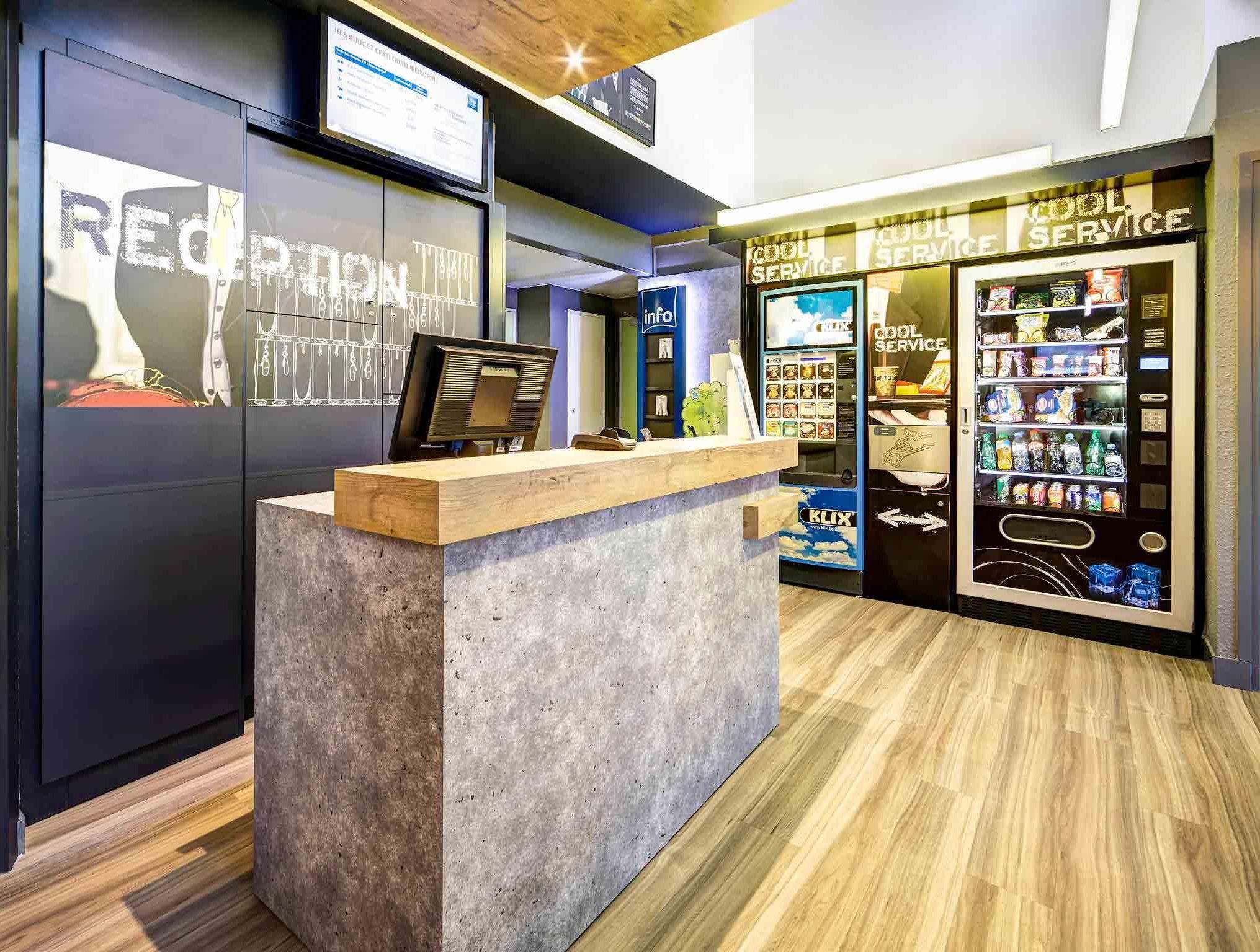 A reception area with a wooden reception desk, a digital screen, and a vending machine labeled 'Cool Service'.