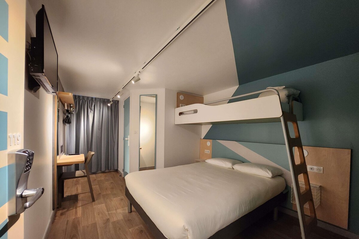 A bunk bed room with a desk, a mirror, and a TV mounted on the wall.