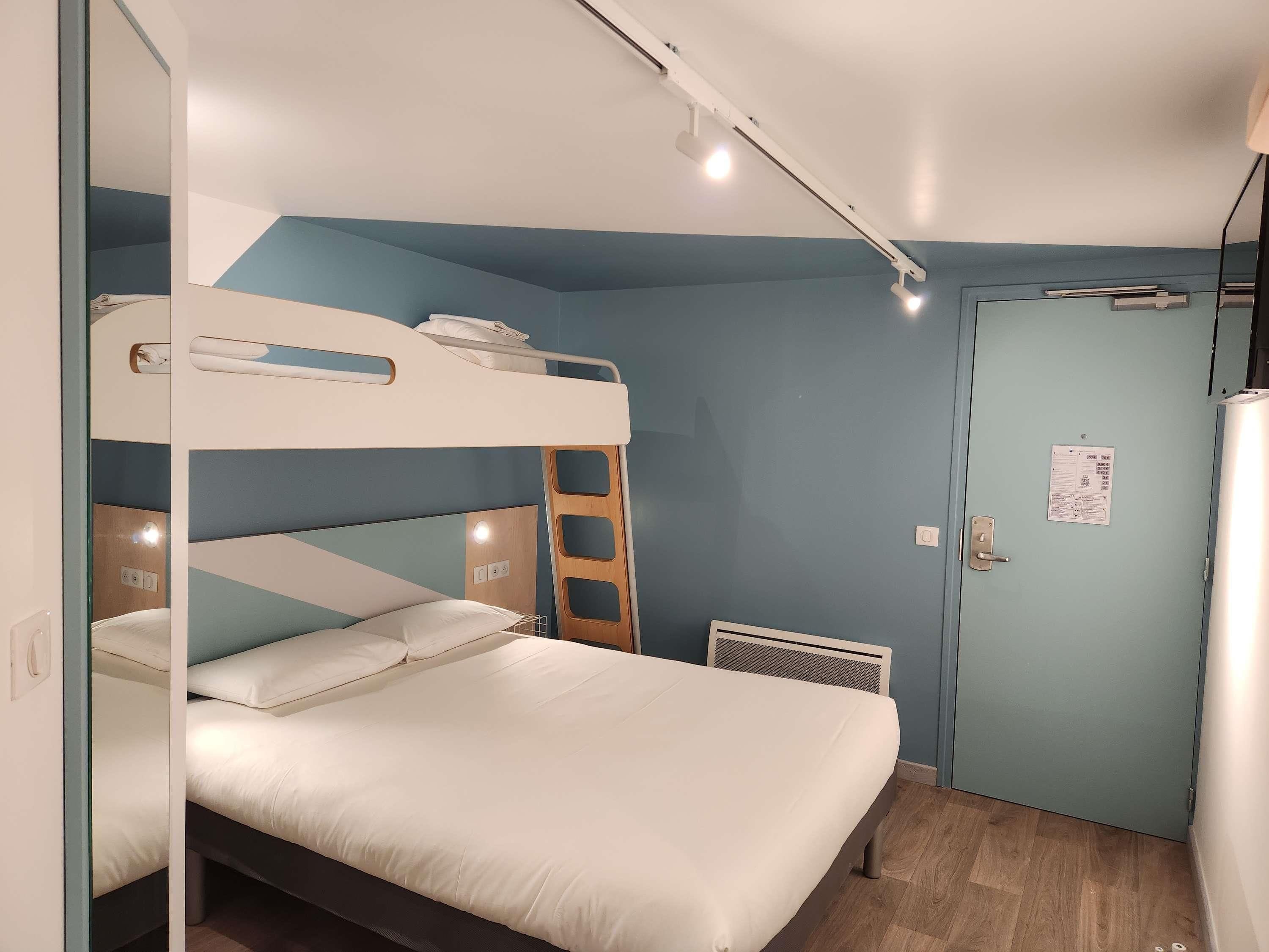 A bunk bed room with a ladder, a desk, and a door with a notice.