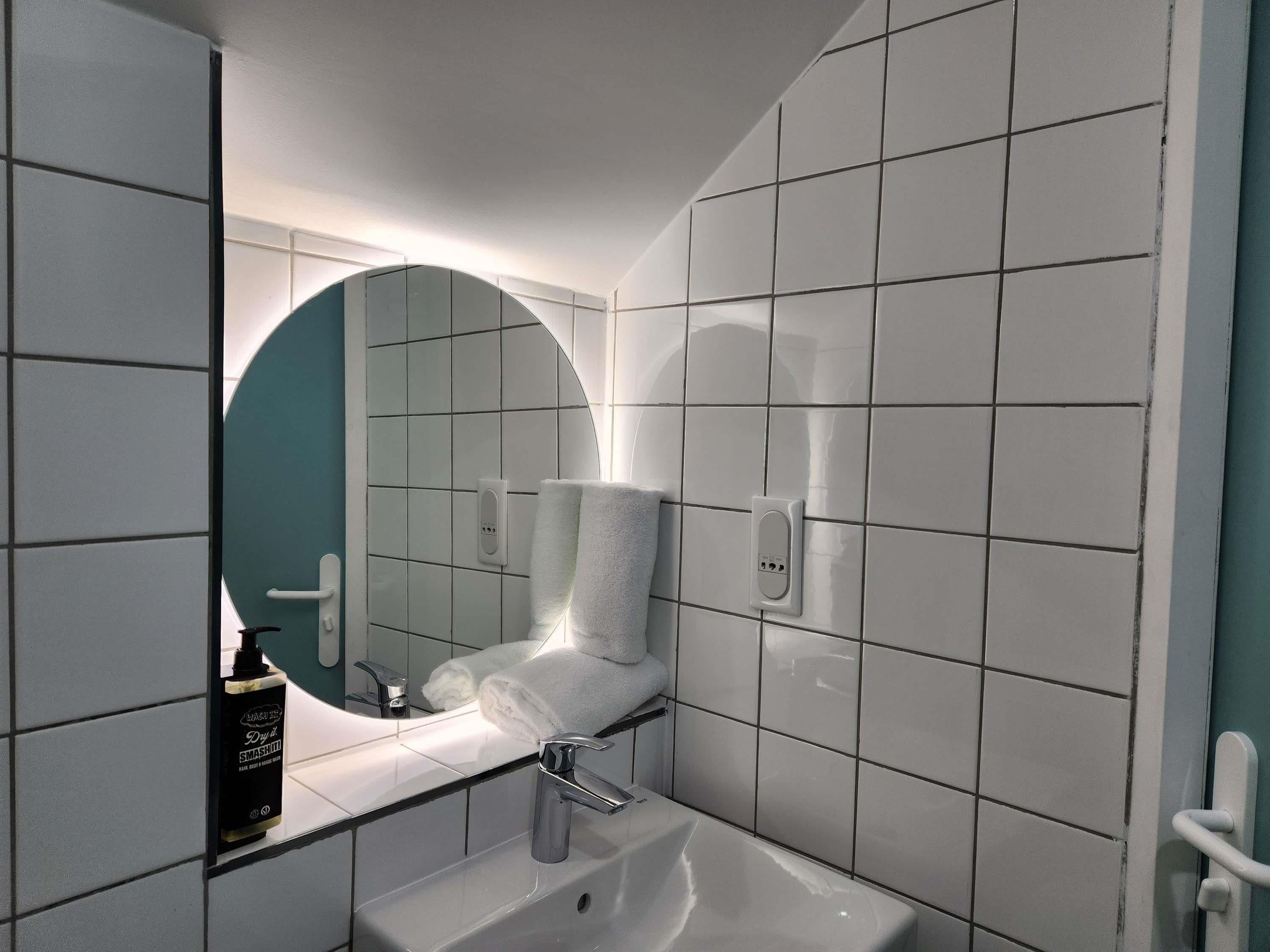 Un baño moderno con un lavabo blanco, un espejo con marco circular y un perchero para toallas.