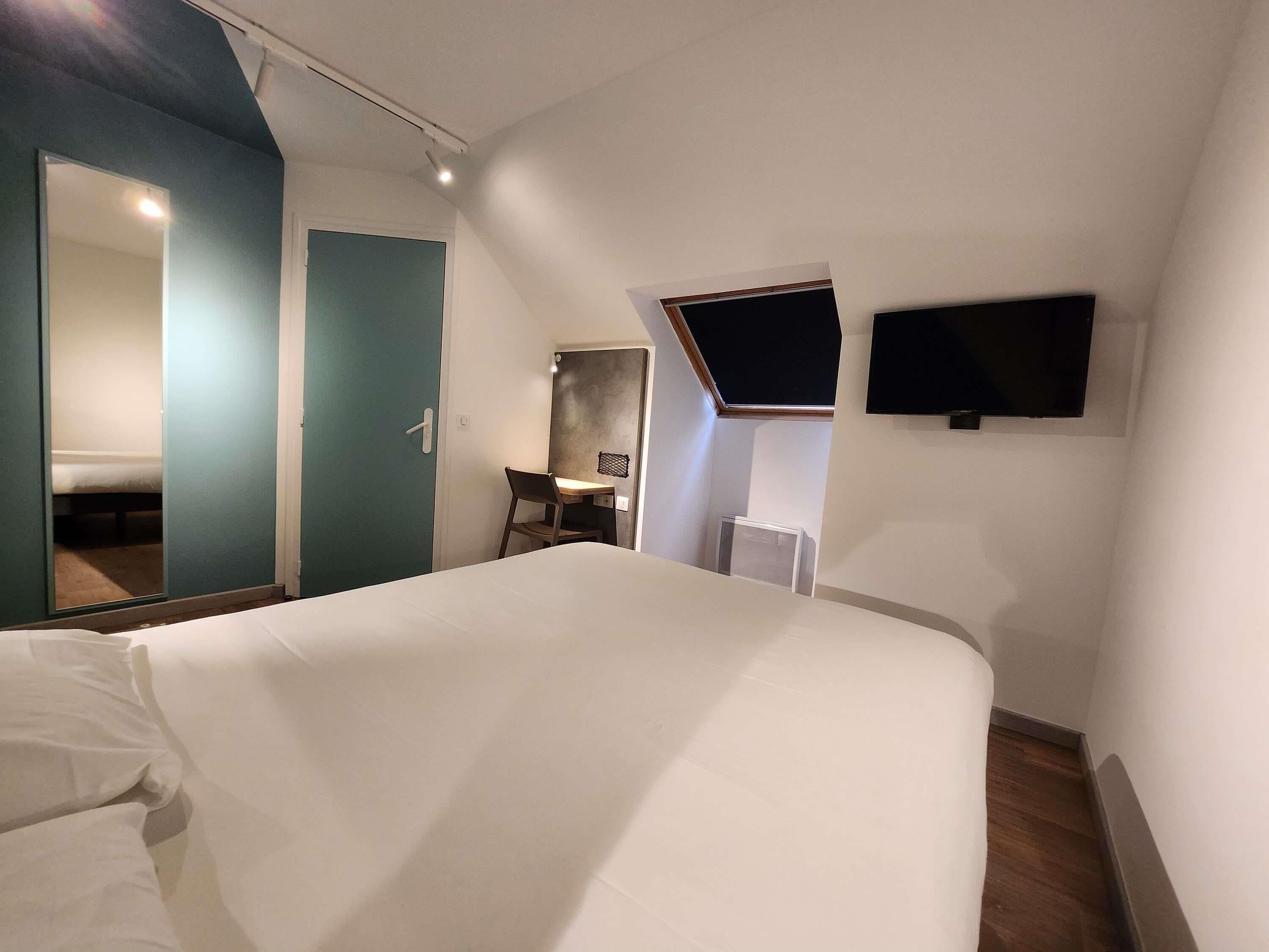 A hotel room with a bed, a desk, a chair, a TV, and a mirror.