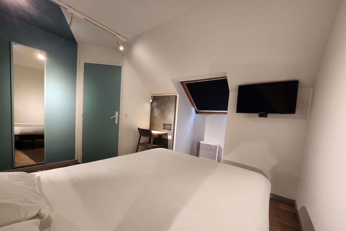 A hotel room with a bed, a desk, a chair, a TV, and a mirror.