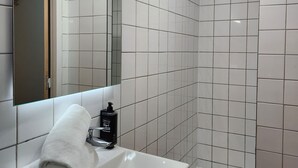 Un baño con lavamanos blanco, espejo y zona de ducha.