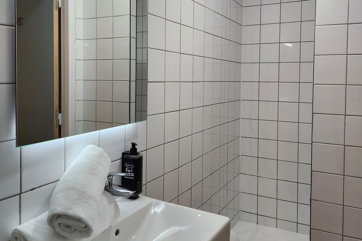 Een badkamer met een wit wastafelmeubel, een spiegel en een douchehoek.