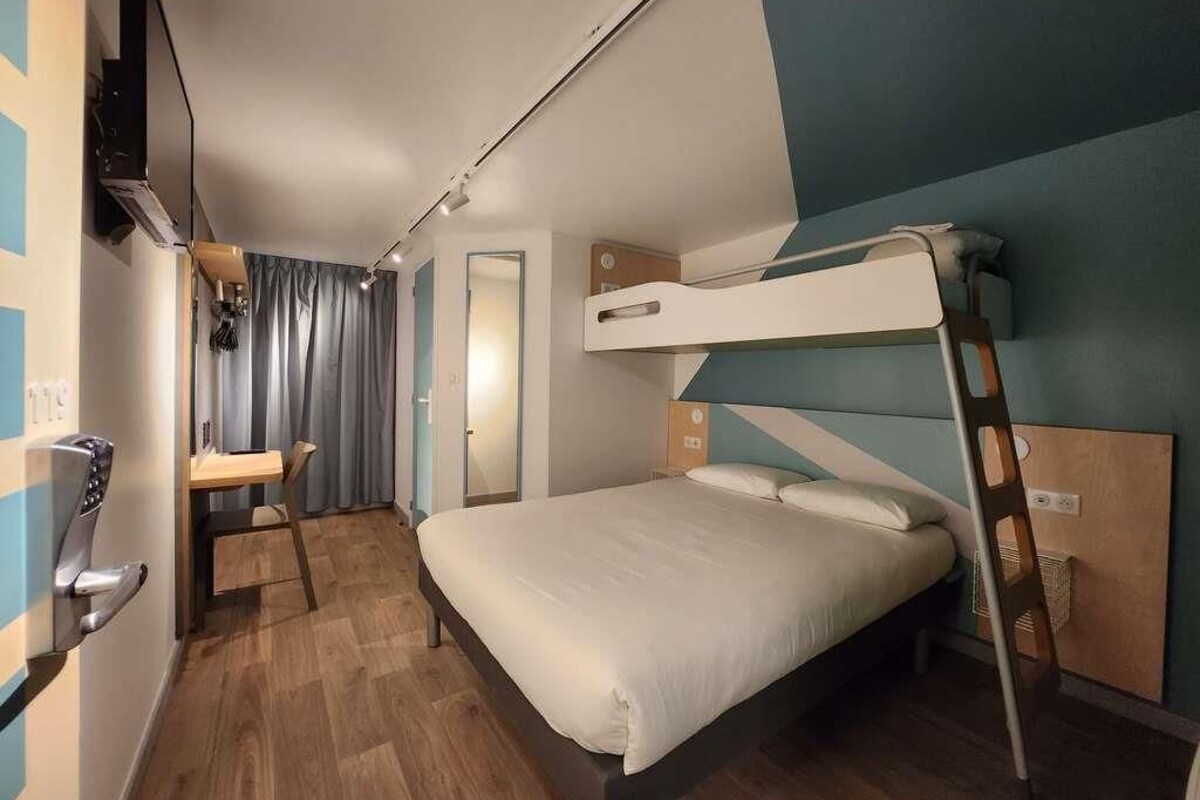 Een slaapkamer met stapelbed, bureau, televisie aan de muur en een houten vloer.