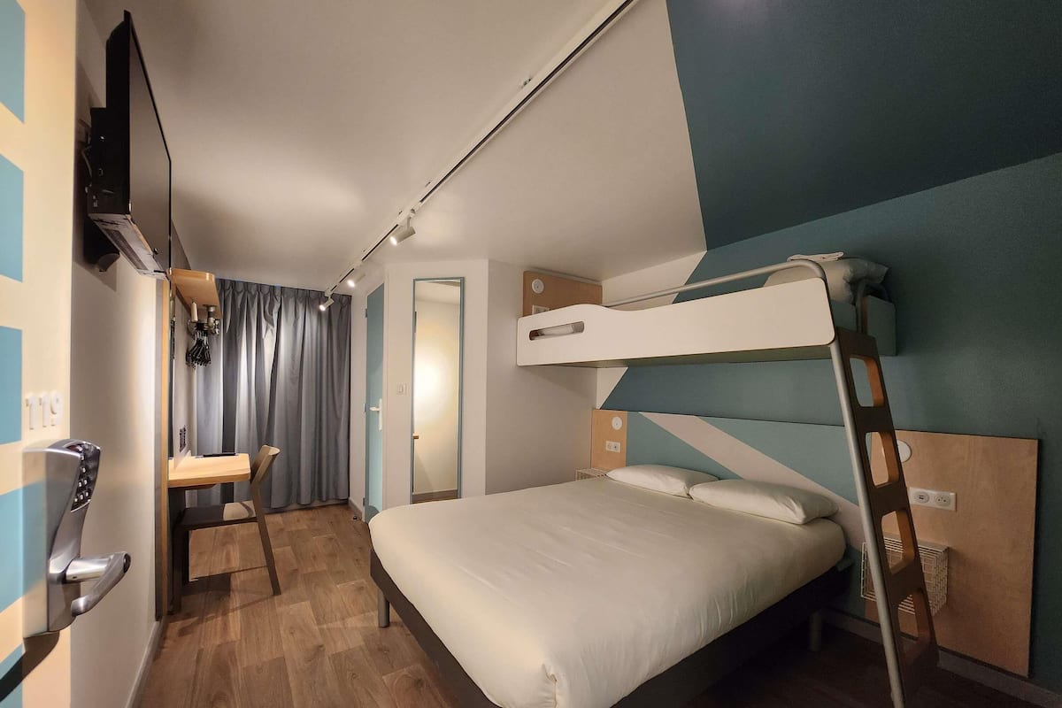 A bunk bed room with a desk, a mirror, and a TV mounted on the wall.