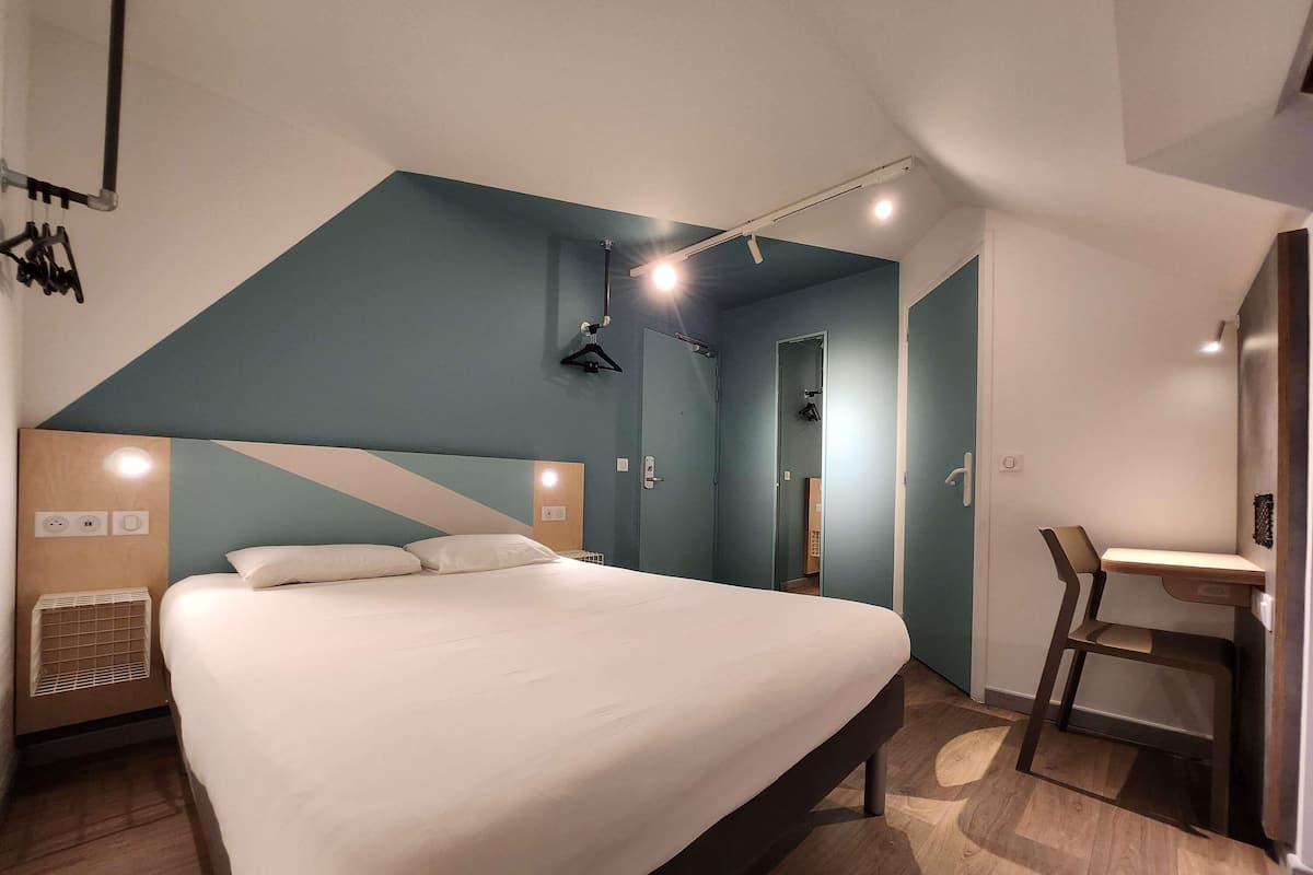 A modern hotel room with a large bed, a desk, and a chair.