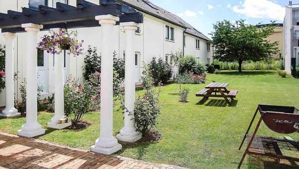 Un edificio blanco con jardín, una mesa de picnic y una parrilla.